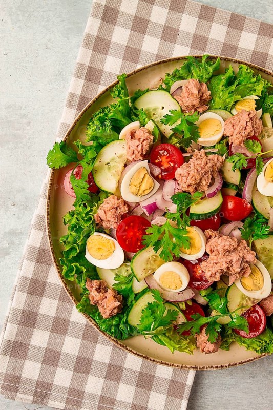 Tuna salad, vegetable salad with quail eggs, lettuce, red onion and cucumbers, on a light gray table, keto food, lifestyle, healthy eating, selective focus, top view, no people