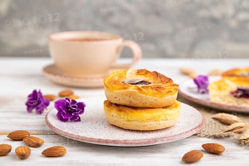 Small cheesecakes with jam and almonds with cup of coffee on a white wooden background and linen textile. Side view, close up, selective focus