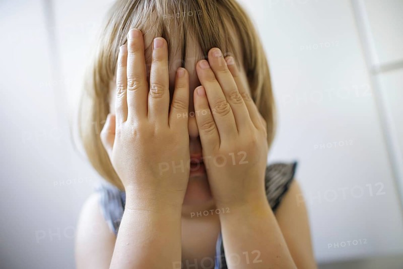 Symbolic photo on the subject of fear in children (posed scene) . A little girl holds her hands in front of her face and is afraid. Berlin, 21.08.2024