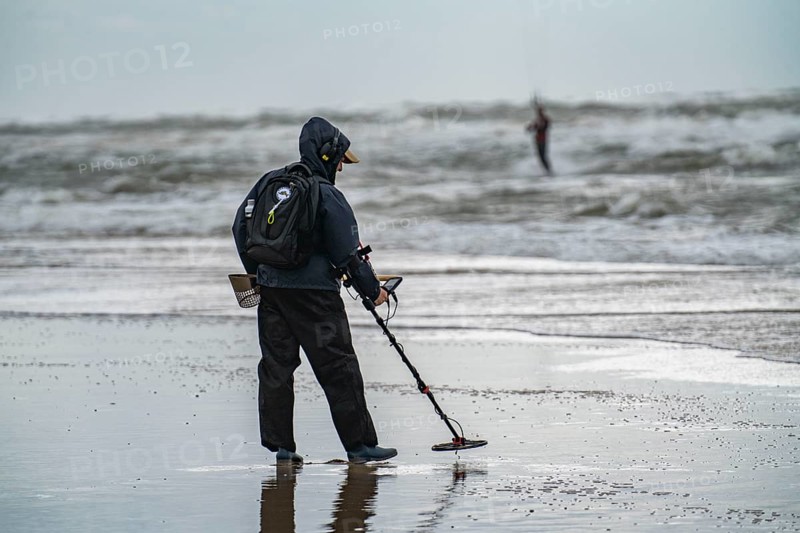 Treasure hunter, man with metal detector on the beach, dark storm clouds, autumn at the North Sea in North Holland, near Egmond aan Zee, Netherlands