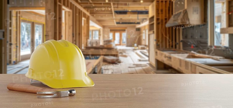 Yellow hard hat and hammer on a wood background with home renovation in construction site in the background