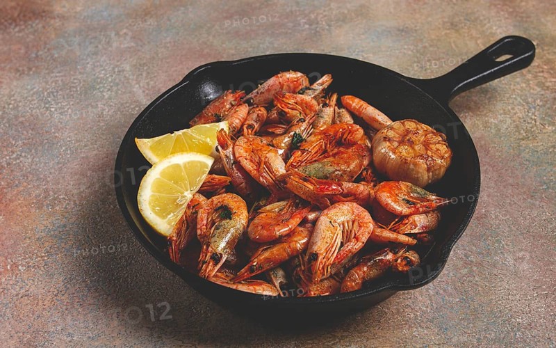 Fried shrimps, in a cast-iron pan, shrimps for beer, in a newspaper, on a gray table, there are no people