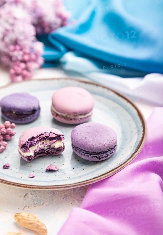 Purple macarons or macaroons cakes with cup of coffee on a white concrete background and magenta-blue textile. Side view, close up, selective focus