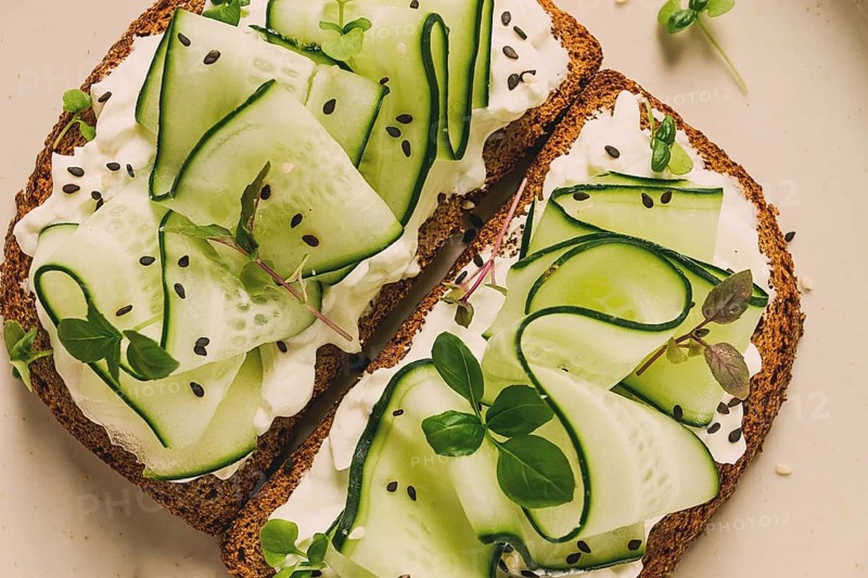 Breakfast, cereal bread sandwiches, cream cheese, sliced cucumber, with micro greenery on a light table, close-up, top view, selective focus, no people