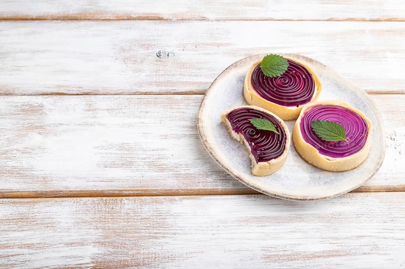 Sweet tartlets with jelly and milk cream on a white wooden background. Side view, copy space