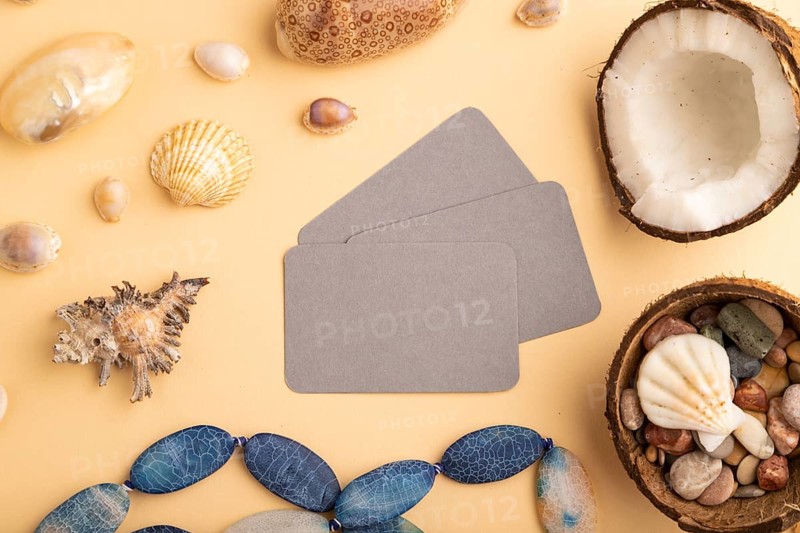 Brown paper business card with coconut, seashells, pebbles, beads on orange pastel background. Top view, flat lay, copy space. Tropical, healthy food, vacation, holidays concept