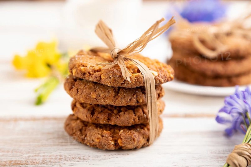 Oatmeal cookies with spring snowdrop flowers bluebells, narcissus and cup of coffee on white wooden background. side view, close up, defocused, still life. Breakfast, morning, spring concept