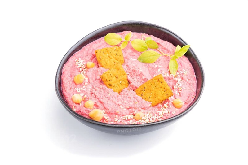 Hummus with beet and microgreen basil sprouts in ceramic bowl isolated on white background. Side view, close up