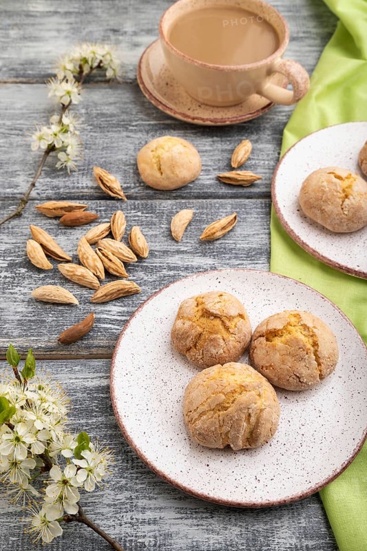 Almond cookies and a cup of coffee on a gray wooden background and green linen textile. Side view, close up