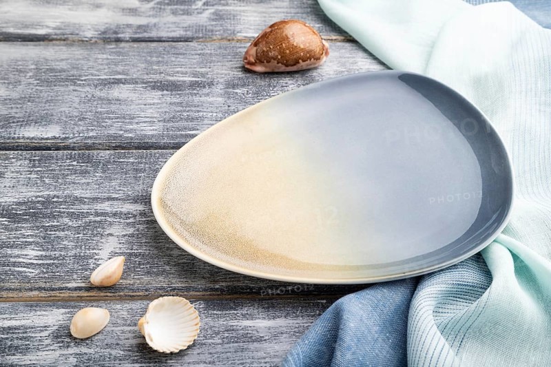 Empty blue ceramic plate on gray wooden background and blue textile. Side view, close up