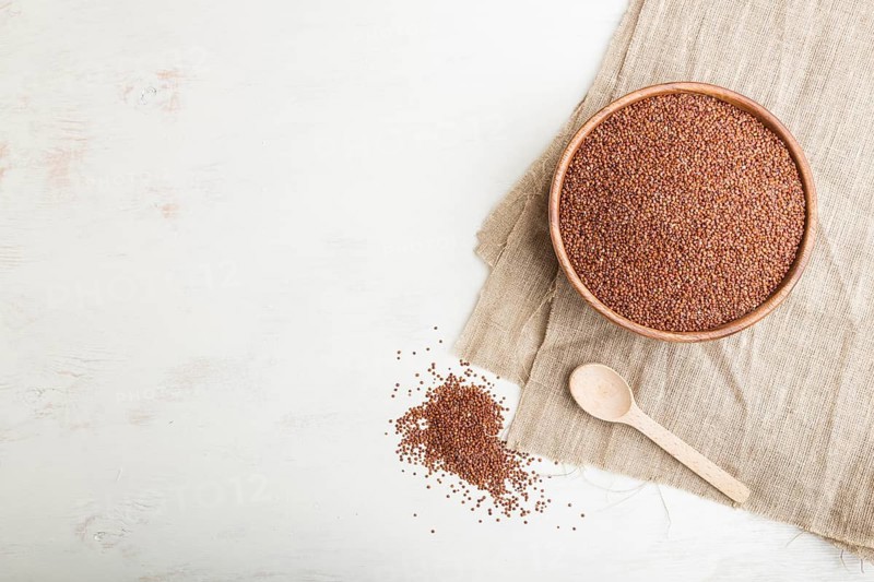 Wooden bowl with raw red quinoa seeds on a white wooden background and linen textile. Top view, flat lay, copy space