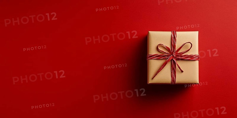 Banner with small Christmas gift box wrapped in kraft paper on red background with copy space. Generative Ai, AI generated