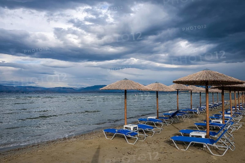 Kalamaki, Corfu, Greece, Sun loungers and parasols on Kalamaki beach in the north-east of the Greek island of Corfu. In the background mainland Albania with the seaside resort of Saranda, Europe