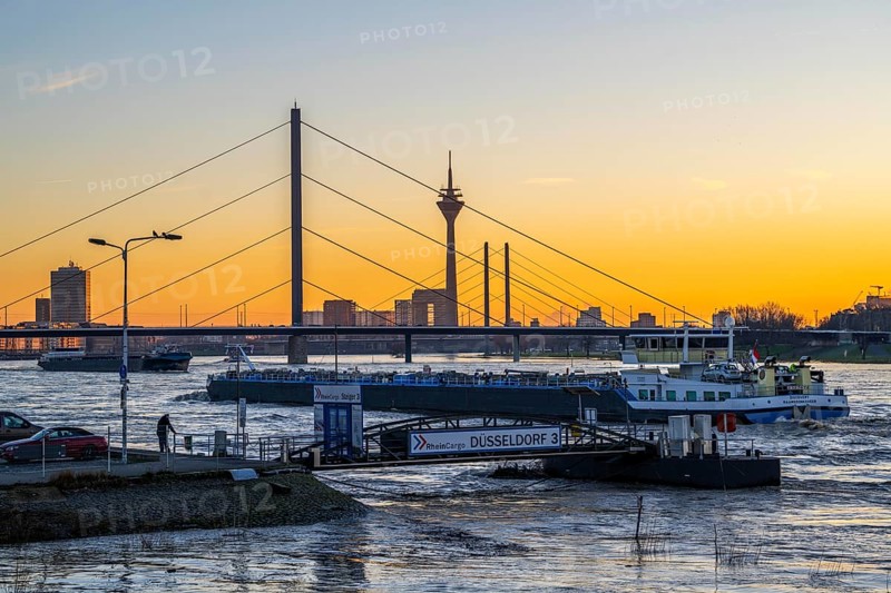 Sunset on the Rhine near Düsseldorf, skyline of the city centre with Rhine Tower, Rheinkniebrücke, behind, Oberkassler Brücke, landing stage at the Rheinterrassen, restaurant ship, cargo ship on the Rhine, North Rhine-Westphalia, Germany, Europe