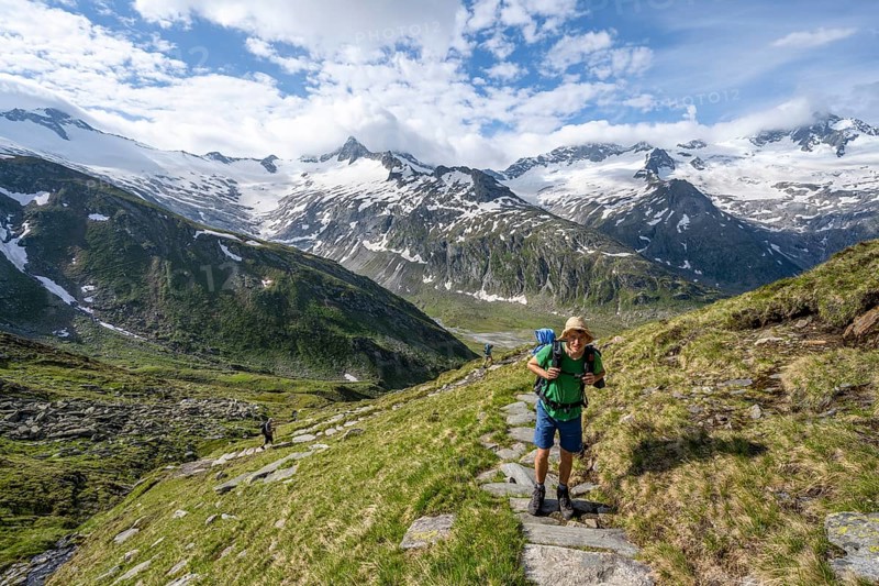 Mountaineer on hiking trail in picturesque mountain landscape, mountain peak with snow and glacier Schwarzensteinkees, Hornkees and Waxeggkees, summit Schwarzenstein, Hornspitzen and Großer Möseler, Berliner Höhenweg, Zillertal Alps, Tyrol, Austria, Europe
