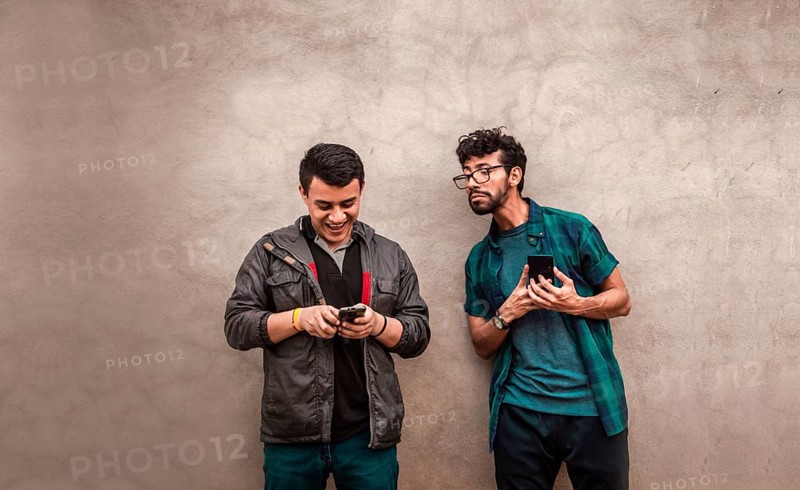 Man spying on another guy cell phone near him. Gossipy man spying on his friend cell phone. Man spying on his friend cell phone near him