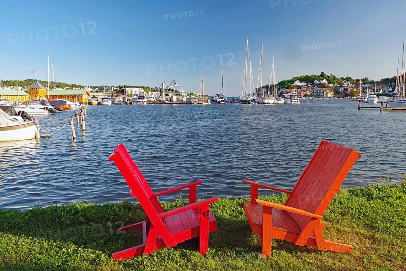 Two red wooden chairs on a lawn overlooking a sunny harbour, Sandefjord, Norway, Europe