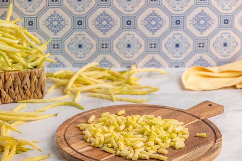 Sliced yellow beans on a wooden chopping board, whole runner beans in the background