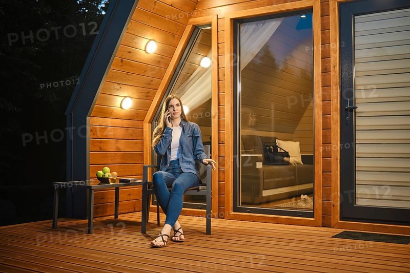 Late at night a girl sits on the terrace of a tiny house and talks on the smartphone with her parents due to the time zone difference