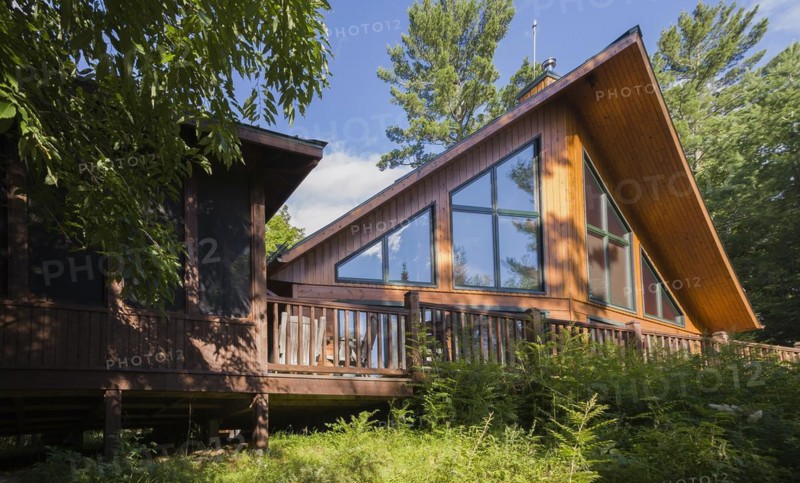 Back view of a milled cottage style flat log profile home with elevated wooden deck and landscaping in summer, Quebec, Canada, North America