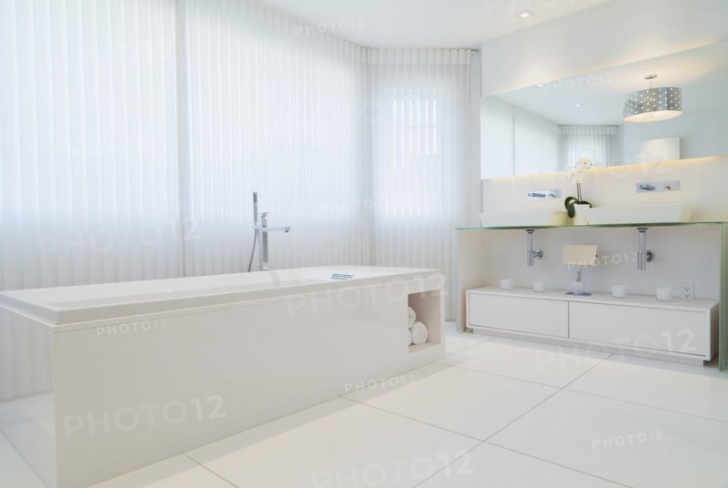 White elongated rectangular bathtub and cabinets with large wall mirror in en suite with ceramic tile flooring on upstairs floor inside a luxurious residential home, Quebec, Canada, North America