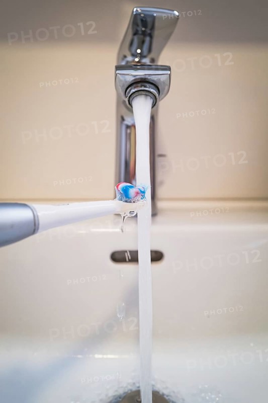 A bathroom tap is running while a toothbrush is held under the running water, symbolic image of water consumption