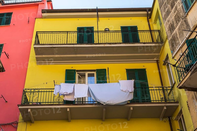 Yellow residential apartment building facade with washed clothes and blue bed sheet drying on clothesline in Riomaggiore, Cinque Terre, La Spezia province, Italy, Europe