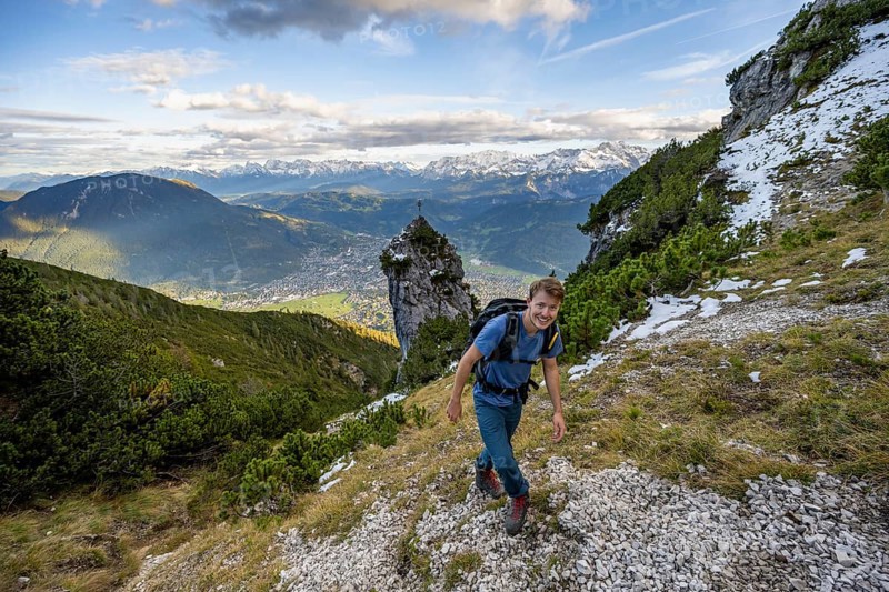 Mountaineers on a hiking trail, rocky peak with summit cross in the background, view of Garmisch-Partenkirchen and mountain panorama, hike to Kramerspitz, in autumn, Ammergau Alps, in autumn, Bavarian Alps, Bavaria, Germany, Europe