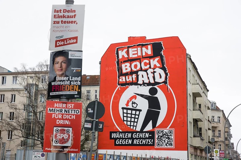 Kein buck auf AfD / Wählen gehen - gegen rechts! is the text on an oversized mural on the wall of a building on Karl-Marx-Straße in Berlin Neukölln. The mural was created by the Kein buck auf Nazis initiative, which has been in existence since 2016. In the foreground, election posters for the parties Die Linke (If your shopping is too expensive, a corporation will cash in), BSW (Our country wants peace.) and SPD (Here's more net for you.) hang on a lamp post. Berlin, 01.02.2025