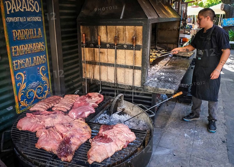 La Boca, Buenos Aires, Argentina, Argentine assado, grill restaurant Parrilla, a grill master prepares assado, steaks and sausages, on the grill. La Boca, colourfully painted houses in the harbour district around the El Caminito alley. La Boca emerged at the end of the 19th century as a neighbourhood of Italian immigrants, most of whom worked as industrial workers. Today, the working-class neighbourhood is popular with tourists, partly because of its original houses, often built from the sheet metal of scrapped ships and brightly painted with ship paint, South America