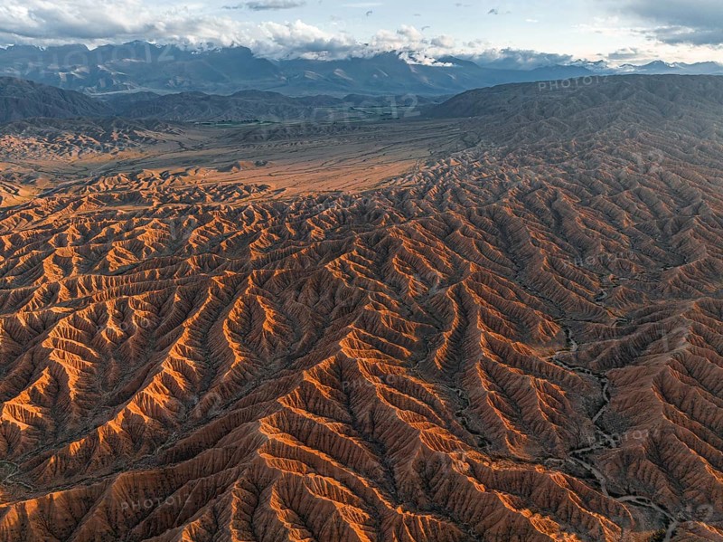 Landscape of eroded hills, badlands at sunset, mountain peaks of the Tian Shan Mountains in the background, aerial view, Canyon of the Forgotten Rivers, Issyk Kul, Kyrgyzstan, Asia