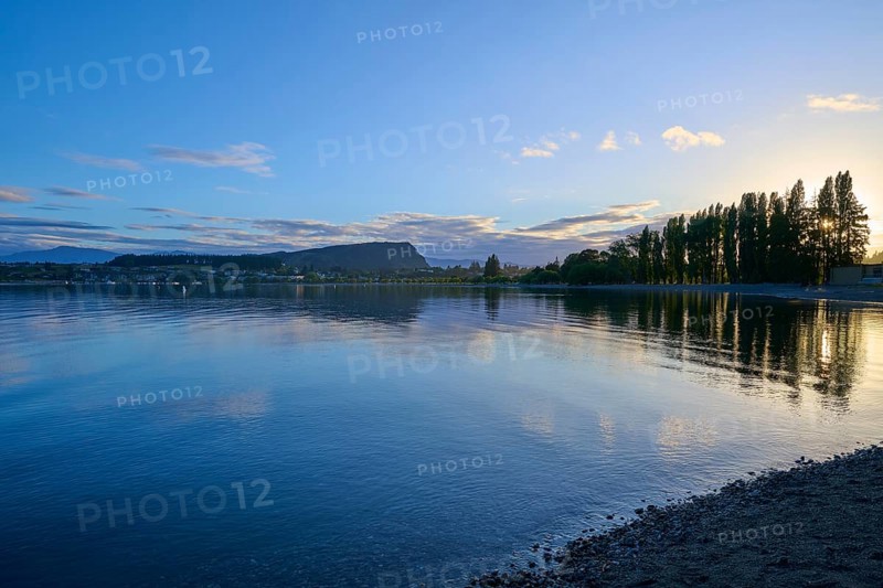 Clear lake with trees on the shore, sunrise and cloudy sky, calm scenery, summer, Lake Wanaka, Wanaka, Otago, South Island, New Zealand, Oceania