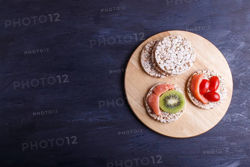 Rice cakes with salmon, kiwi and cherry tomatoes on dark wooden background. top view, copy space
