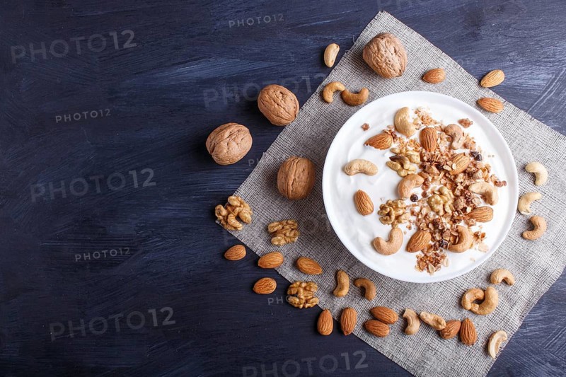 White plate with greek yogurt, granola, almond, cashew, walnuts on black wooden background. top view. copy space