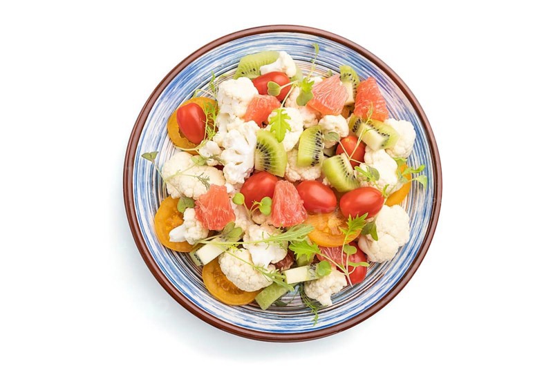 Vegetarian salad of cauliflower cabbage, kiwi, tomatoes, microgreen sprouts isolated on white background. Top view, close up