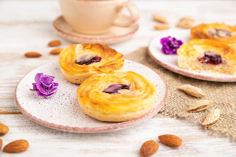 Small cheesecakes with jam and almonds with cup of coffee on a white wooden background and linen textile. Side view, close up, selective focus