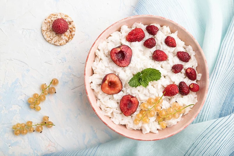 Rice flakes porridge with milk and strawberry in ceramic bowl on white concrete background and blue linen textile. Top view, flat lay, close up