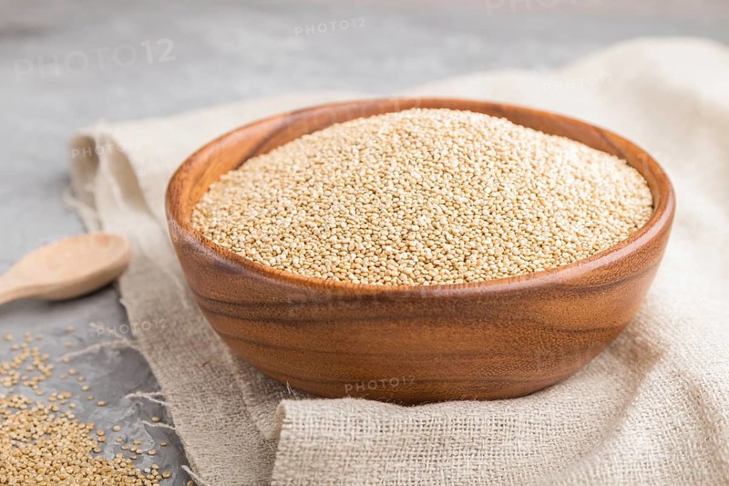 Wooden bowl with raw white quinoa seeds and wooden spoon on a gray concrete background and linen textile. Side view, close up, selective focus