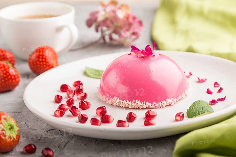 Pink mousse cake with strawberry and a cup of coffee on a gray concrete background and green textile. side view, close up, selective focus