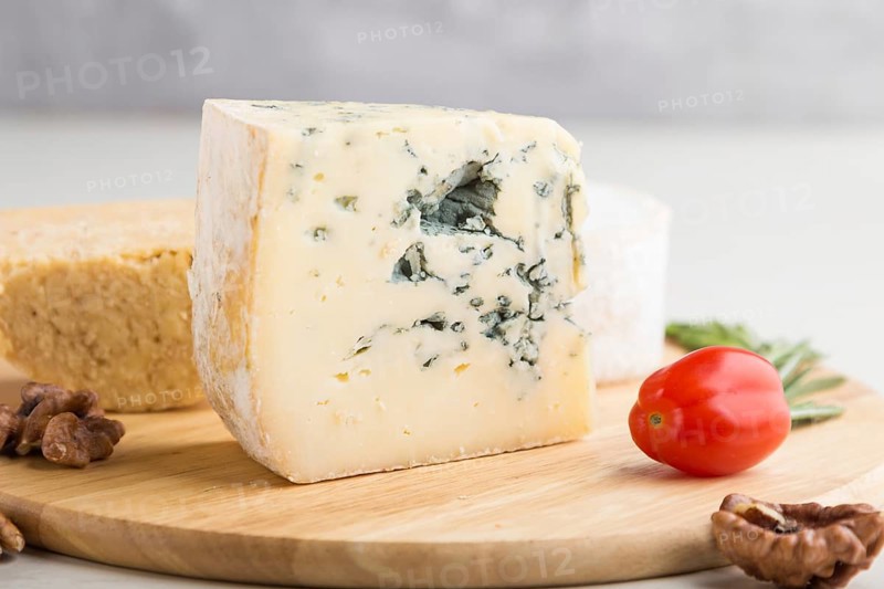 Blue cheese and various types of cheese with rosemary and tomatoes on wooden board on a white wooden background. Side view, close up, selective focus