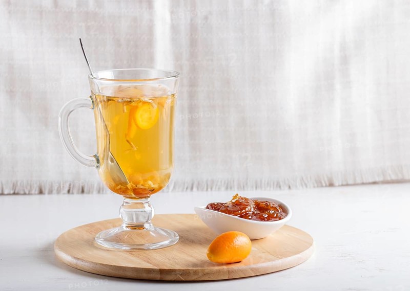 Jasmine tea with kumquat in a glass cup on a wooden board on a white background. close up, copy space