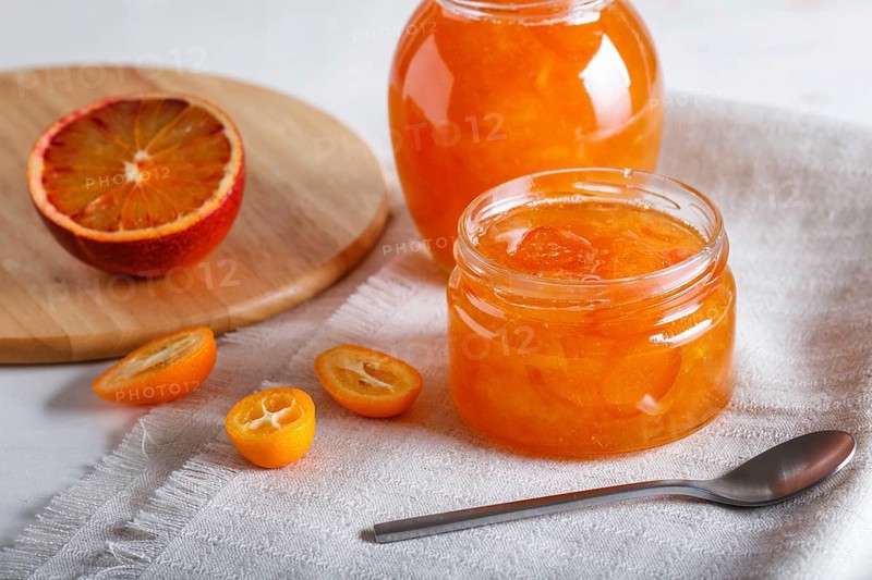 Orange and kumquat jam in a glass jar with fresh fruits on a white linen tablecloth. Homemade, close up