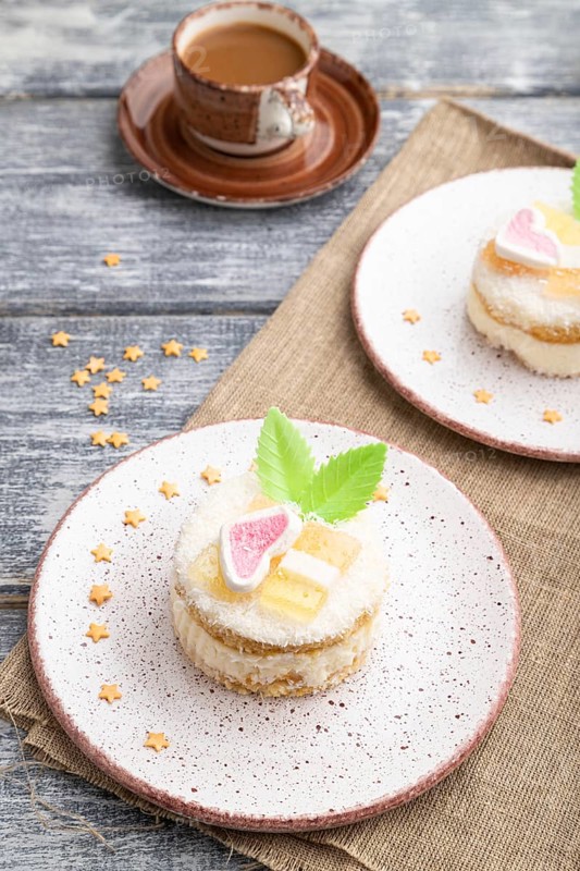 Decorated cake with milk and coconut cream with cup of coffee on a gray wooden background and linen textile. Side view, close up