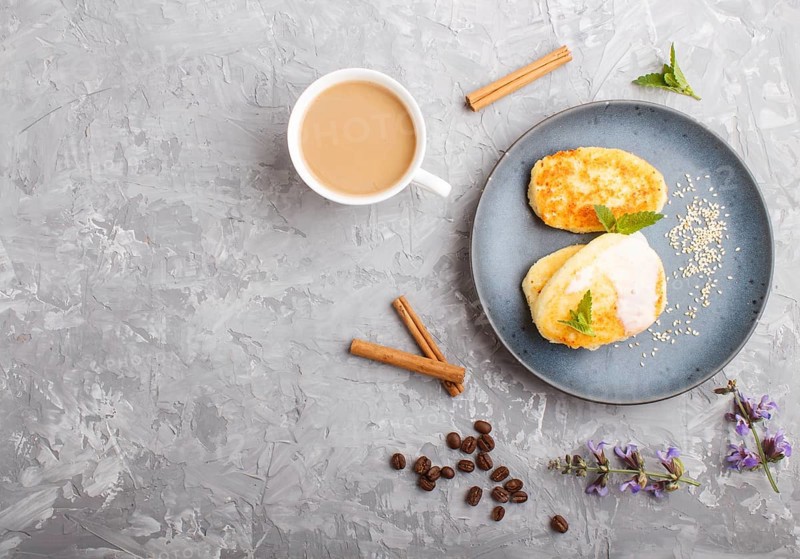 Cheese pancakes on a blue ceramic plate and a cup of coffee on a gray concrete background. top view, flat lay, copy space