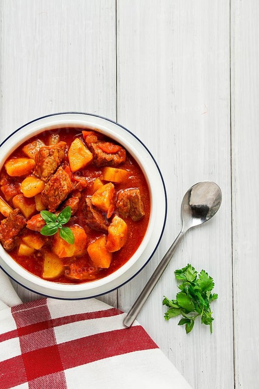 Potatoes stewed with meat, in tomato sauce, with spices and herbs, no people, on a white table