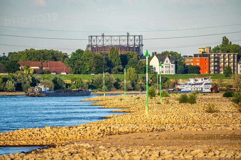 Cargo ship at low water on the Rhine near Duisburg-Homberg, view of Duisburg-Laar, houses on Deichstraße, gasometer of ArcelorMittal Hochfeld GmbH steel wire plant, 3.48 metres is normal, at the time of the photo only 2.58 metres level, but still far from the low level when restrictions for shipping enter, North Rhine-Westphalia, Germany, Europe