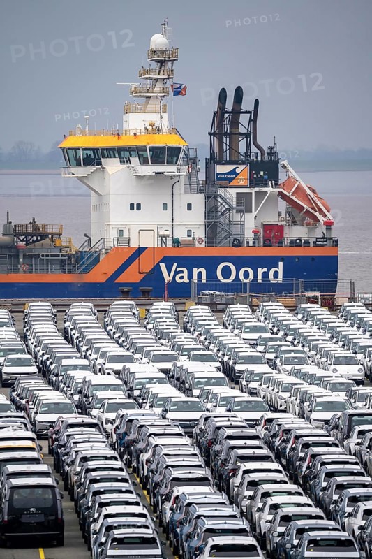 Parking space for import vehicles, hundreds of Hyundai Ioniq, electric cars, waiting for onward transport, behind them, on the Weser, the dredger, the hopper dredger, suction dredger, Vox Ariane, which holds the tug to a certain depth, at the EUROGATE container terminal in the overseas port of Bremerhaven, Lower Saxony, Germany, Europe