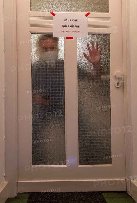 Symbolic image Domestic quarantine, man is in isolation at home due to a suspected corona infection, warning sign for visitors on the front door, communicating with a visitor through the door