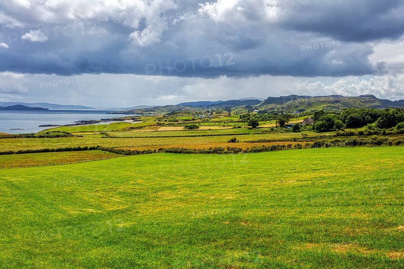 Extensive coastal landscape with sea, meadows and cloudy skies, near the Great Pollet Sea Arch