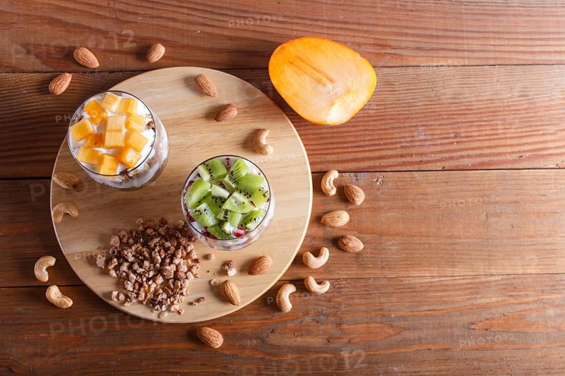 Dessert with greek yogurt, granola, almond, cashew, kiwi and persimmon on brown wooden background. top view, copy space